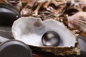 Image of a black pearl in the shell on wet pebbles.