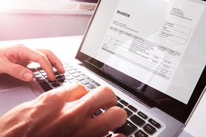 Businessman's Hands Working On Invoice On Laptop
