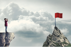 person looking across to a red flag on a mountain top